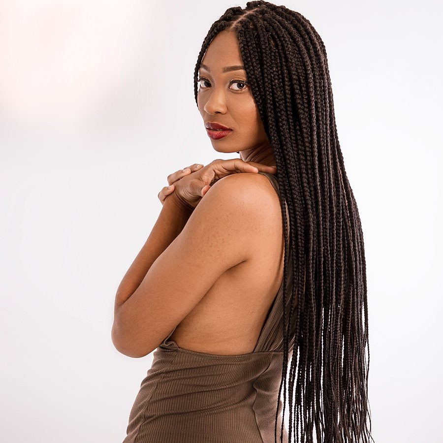Licensed stock photograph: a Black woman in a studio, long box braids falling past her shoulders as she looks back.